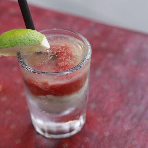 A layered red and white frozen drink with a lime wedge and black straw on a red table.