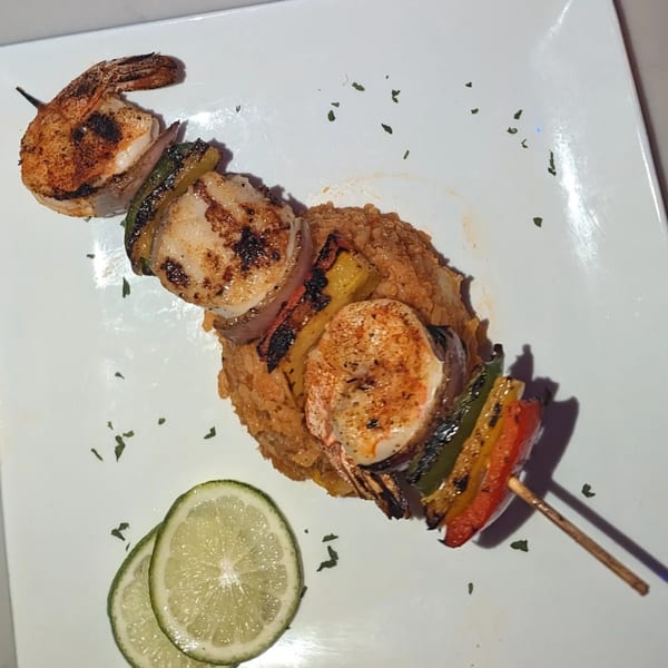 Grilled shrimp and scallop skewer with bell peppers and onions, served over rice with lime slices.