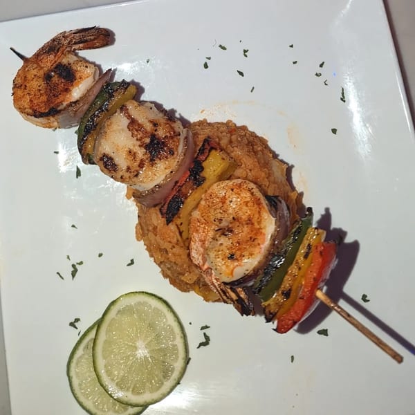 Grilled shrimp and scallop skewer with bell peppers and onions, served over rice with lime slices.