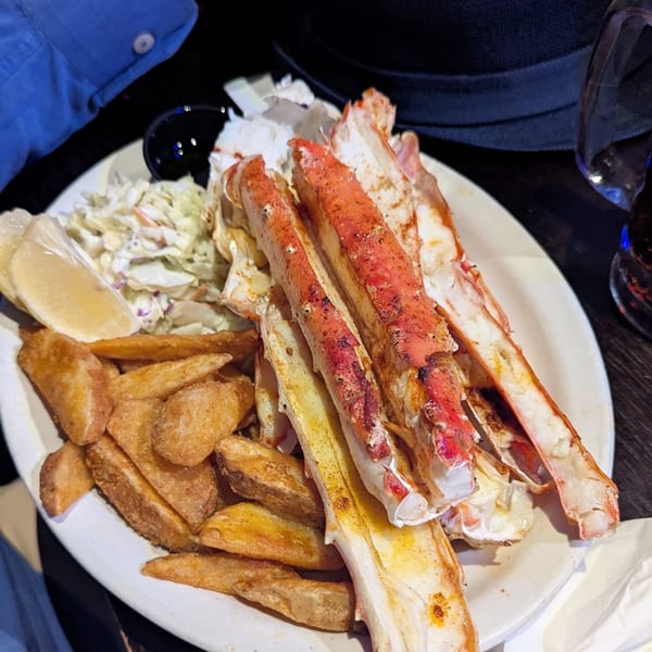 A plate of crab legs, coleslaw, and potato wedges from Fisherman's Market & Grill.