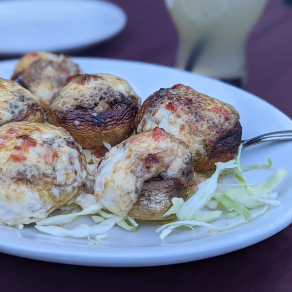 Six baked stuffed mushrooms with melted cheese and red peppers, garnished with shredded lettuce.