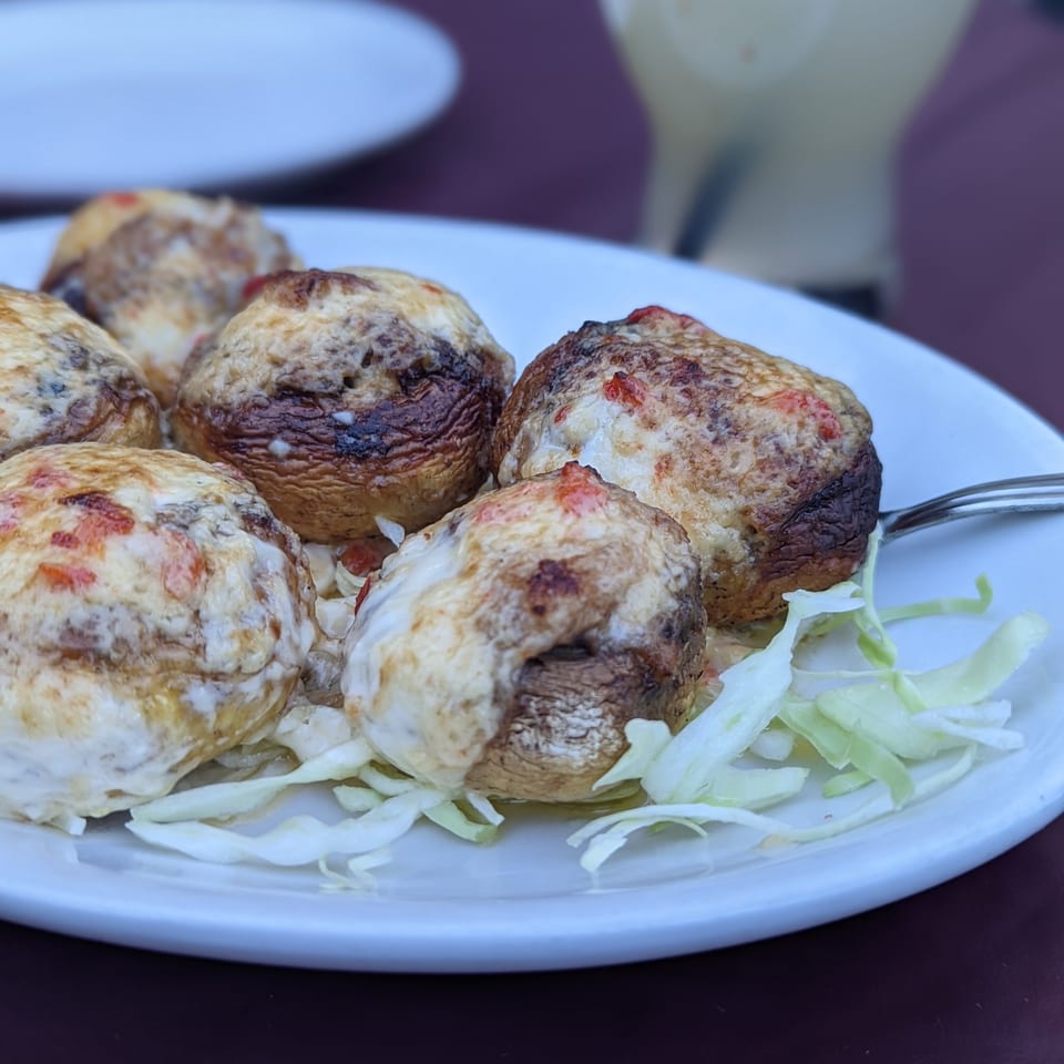 Six baked stuffed mushrooms with melted cheese and red peppers, garnished with shredded lettuce.