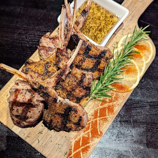 Grilled lamb chops with rosemary, lemon slices, and a side of mustard on a wooden board.