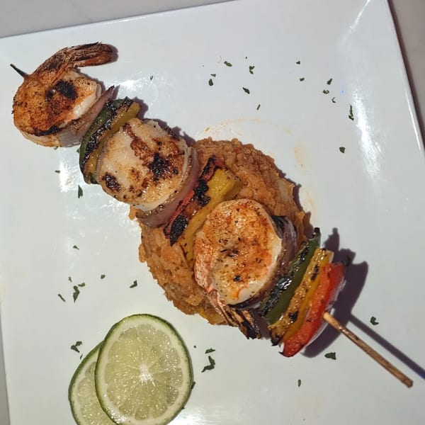 Grilled shrimp and vegetable skewer over rice, garnished with lime slices on a white plate.