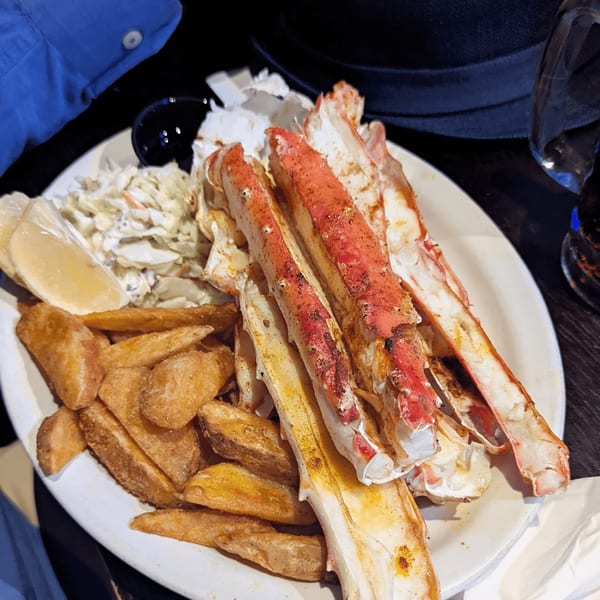 A plate of crab legs, french fries, coleslaw, and a lemon wedge from Fisherman's Market & Grill.