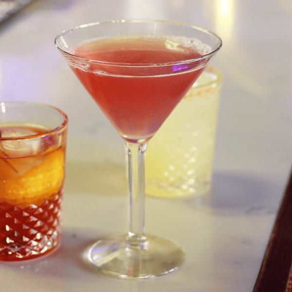 A vibrant red cocktail in a martini glass, with another drink in a patterned glass beside it.
