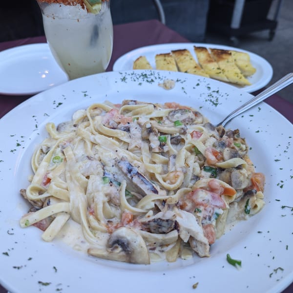 Creamy seafood fettuccine with mushrooms and tomatoes, garlic bread, and a cocktail at Fisherman's Market & Grill.