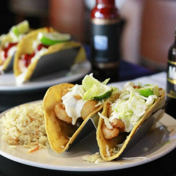 Two shrimp tacos with rice, cabbage, lime, and sauce on a white plate at Fisherman's Market & Grill.